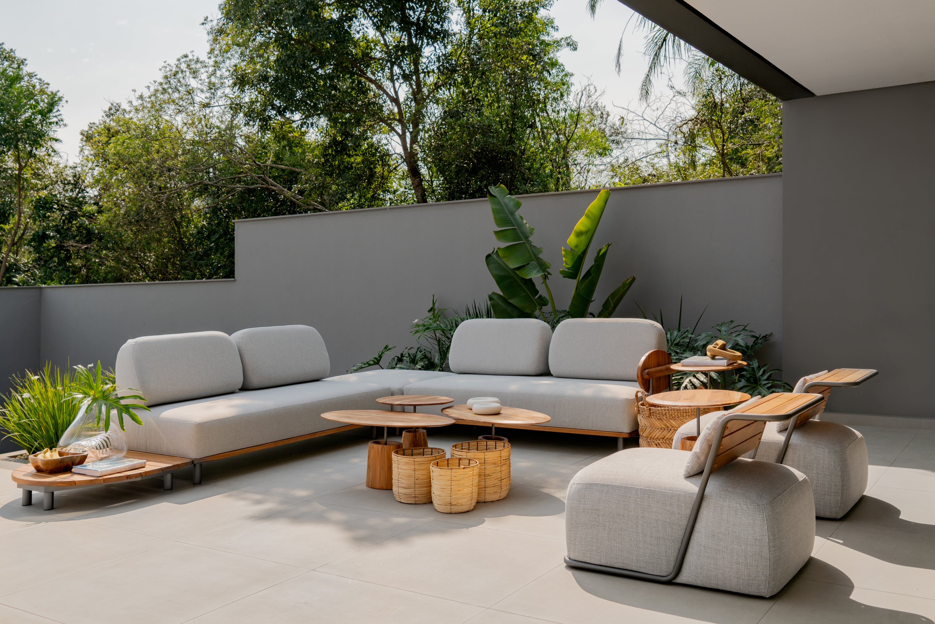Modern outdoor patio with gray sectional sofa, wooden tables, and plants.