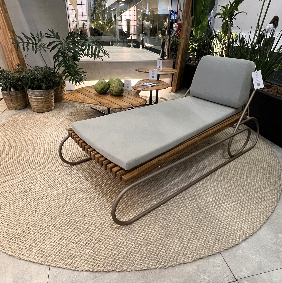 Wooden lounge chair with white cushion on a textured floor, surrounded by plants.