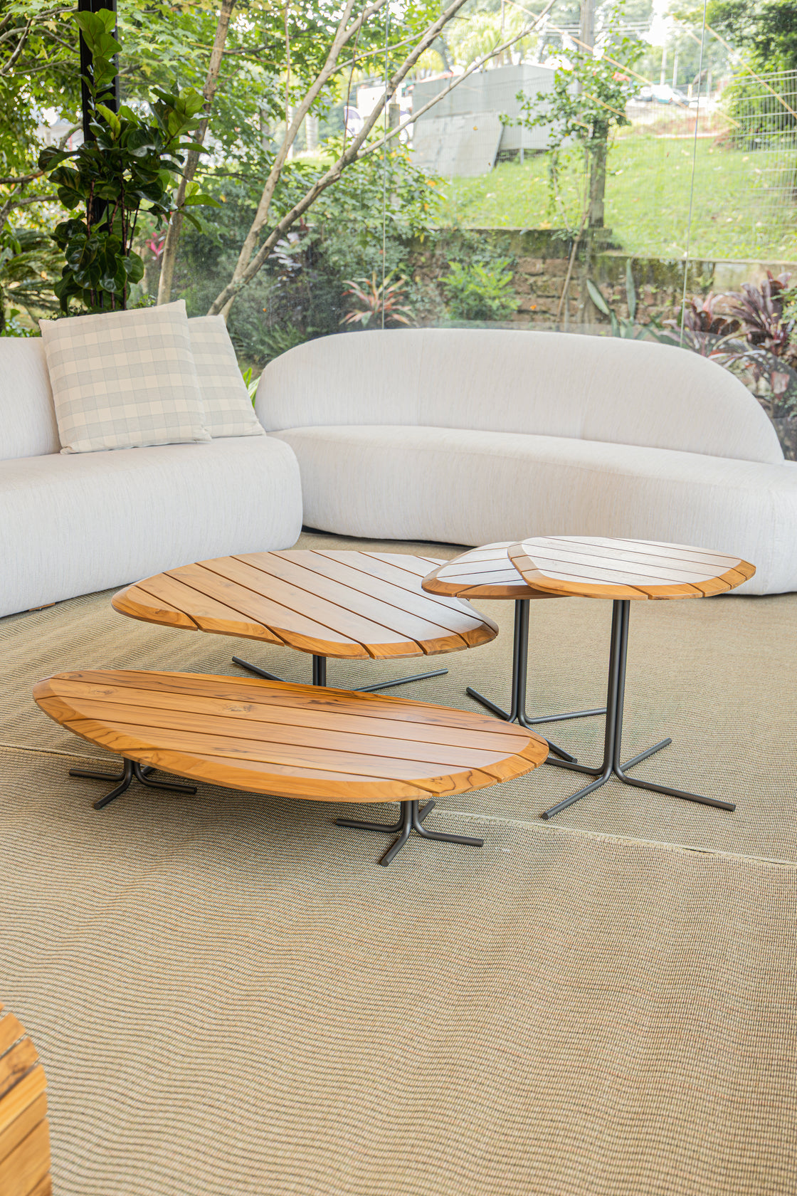 Three oval wooden coffee tables with black metal star legs arranged on a beige textured rug in front of a curved white outdoor sofa.