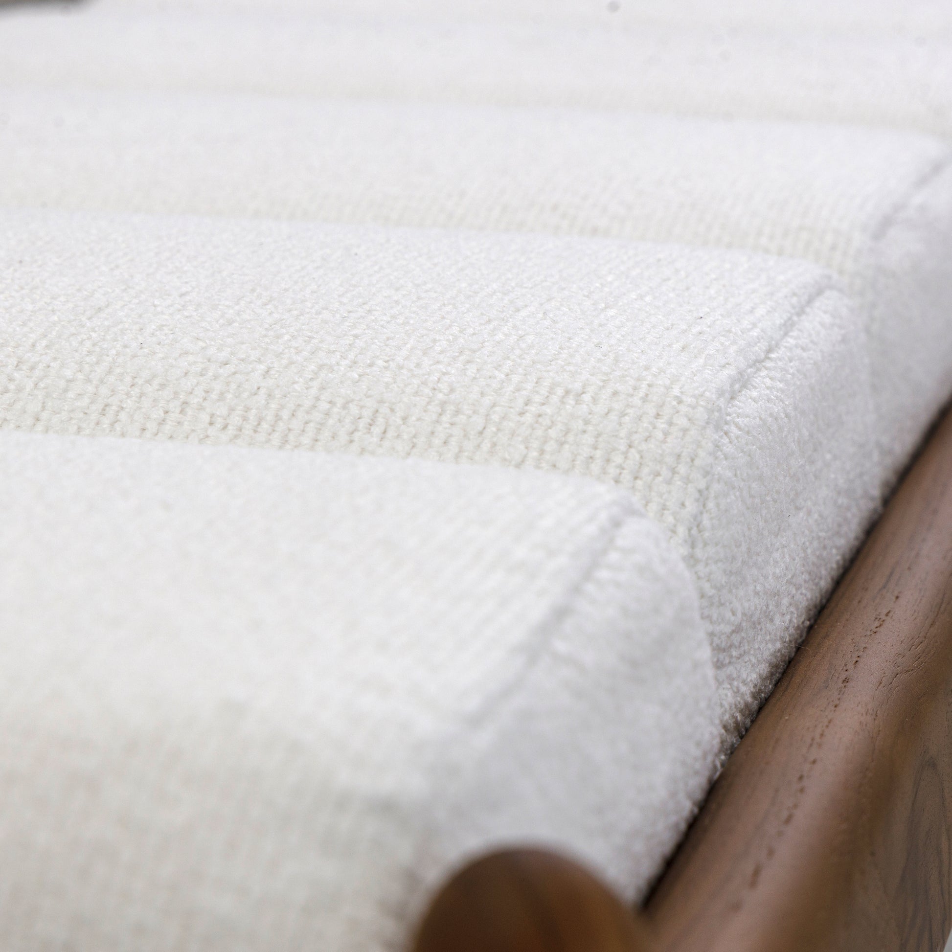 Close-up of a textured white fabric corner with a wooden object partially visible.